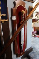 Full view of the sword mounted on a wood plaque with red velvet background. Shows overall display mount and sword sheathed on plaque.