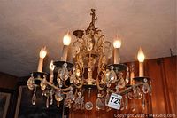 Full view of brass chandelier with candle-style bulbs and faceted glass pendants hanging from ornate scrollwork arms.