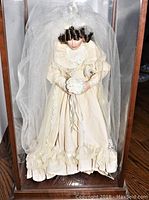 Front view of the bride doll in case showing full dress, veil, and wood-glass display case.