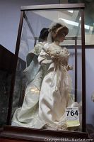 Two Franklin Heirloom porcelain dolls inside a wooden and glass display case from side angle