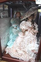 Photo shows two Franklin Heirloom porcelain dolls in Southern Belle style dresses inside a wooden glass-front display case.