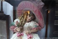 Front view of porcelain doll showing face, bonnet and upper body dressed in white and pink Victorian style dress with ribbons and lace.
