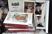 Photo shows Holly the Holiday Bear doll in box, witch or caroler doll in box, and three large hardcover books titled 'Holly'.