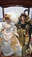 Two Franklin Heirloom porcelain dolls inside a glass display case, both standing side by side with detailed costumes and facial features visible.