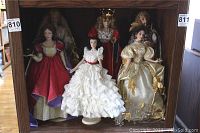 Six Franklin Heirloom porcelain dolls displayed in a cabinet shelf with various period and fantasy costumes.