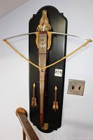 Full frontal view of the decorative crossbow mounted on wooden plaque with two arrows hanging