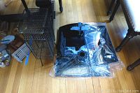 Four items on wooden floor: three black TV mounts or stands, partially disassembled and stacked, and one vintage black metal telephone stand with mesh sides and top rectangular shelf.