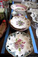 Seven vintage porcelain dishes arranged on dark surface showing gold detailed floral motifs and varying shapes including latticed compote and scalloped plates.