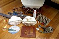Overview of all items in the lot on a wooden floor: nautical and seaside-themed collectibles, decorative pieces, shell motifs, wooden carved plaque, wooden covered wagon model lamp, lighthouse figurine, and other marine themed items.
