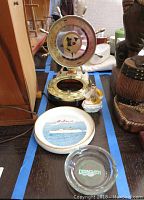 Overview of five nautical items including brass world clock, ceramic dish, ashtray and small figurines on table