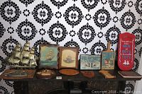 Full view of 12 pieces of wooden plaques and wall decor on a table against a black and white patterned wall, showing various nautical and vintage themes, sizes varying from about 5x8 to 19x9 inches.