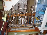 Front view of the wooden model ship showing the full length and masts, mounted on a wooden base.