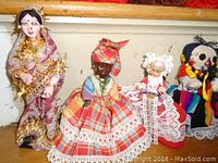 Four multicultural vintage dolls on a shelf showcasing a variety of traditional costumes and facial features.