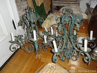 Two matching antique chandeliers with green patina, multiple scroll arms, and candle-style bulb holders shown on wood floor.