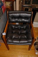 Full frontal view of the Murphy Miller armchair showing black leather seat and back cushions with button tufting and wooden arms and legs.