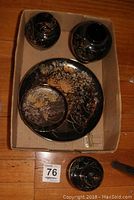 Photo of three black lacquerware ginger jars with lids on two, decorated with gold and red chrysanthemum flowers, along with two matching decorative dishes inside a cardboard box on wooden floor.