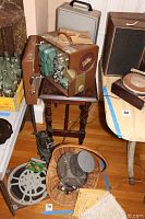 Vintage reel to reel projectors, metal film reels, wicker basket with projector inside, and paper documentation on hardwood floor