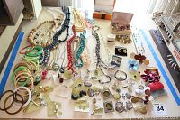Wide view of a large collection of vintage and contemporary costume jewelry including necklaces, bangles, earrings, pendants, and boxed sets on a white table.