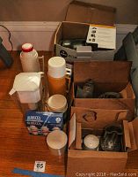 View of Tassimo coffee maker in box, thermoses, Brita filters, vintage Universal wall mount grinder, food processor parts and small items arranged on a table.