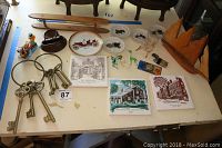Table display of large brass skeleton keys, glass animals, collectible plates, souvenir trivets, and various small items