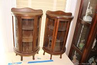 Two matching wood and glass curio cabinets side by side with curved glass fronts and wooden frames.