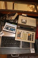 Photo showing Honeywell adding machine with numeric keypad and printer, TI-99 computer keyboard underneath, and an intercom device.