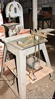 Band saw and planer set placed in a basement with visible wear and dust, showing the full planer with motor and clamps.
