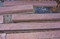 16 reddish-pink granite stone slabs laid out in an outdoor area with visible speckled granite patterning, varying lengths and consistent thickness.