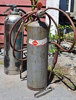 Photo showing the vintage acetylene torch with flammable label and hoses, positioned outdoors against a pole.