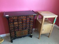 Front view of black-trimmed apothecary chest with 39 drawers and adjacent natural wood side table.