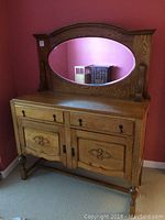 Front view of antique solid oak sideboard with oval beveled mirror, two drawers, and two cabinet doors, showcasing carved features and rounded legs.