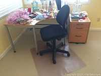View of corner desk in room with file cabinet, chair and carpet protector mat. Desk cluttered with miscellaneous items (not included).