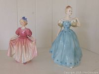 Two Royal Doulton figurines displayed together, showing the full figures and their dress colors.