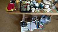 Overview of the assortment showing mugs, cookware, utensils, cookbooks, and bread maker under table