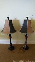 Full view of the pair of matching vintage table lamps with multicolor fabric shades and dark bases on carpeted floor.