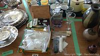 Overview photo of barware items on table including silver trays, glassware, decanter, corkscrews, brushes and coasters.