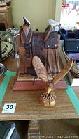Wooden decor items on a table, including a carved olive wood eagle and a carved western saddle on a stand with a plaque.