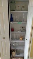 Shelf with assortment of various glass vases including blue vase, small jars, tall clear vases, and gold ceramic cornucopia planter