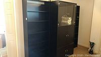 Front view of black shelving unit with several adjustable shelves and one fixed shelf, showing spacious interior.
