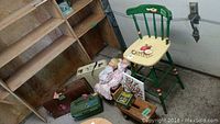 Overview of lot including three vintage suitcases, two dolls, small wooden box, Crayola tin and wooden rocking bassinet.