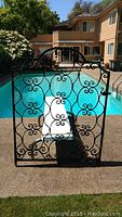 Full front view of gate leaning against a chair by pool, showing entire scrollwork design and curved top.