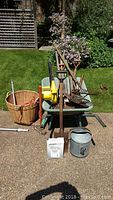 Overview photo of garden tools including wheelbarrow loaded with shovels, rakes, watering can and basket seen in driveway