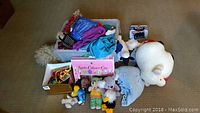 Full view photo of the lot showing multiple plush toys, costumes, Kiddles collector case, and boxes with items on a carpeted floor.