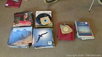 Several stacks of assorted vinyl records on floor showing album covers and record sleeves.