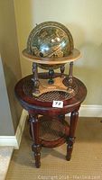 Full view of round accent table with caned top and lower shelf, wooden desk globe placed on top
