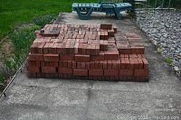 Front view of over 500 red clay bricks stacked neatly on a concrete patio.