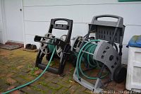 Side view showing two hose reels with green hoses on wheeled rolling stands outside against a white siding wall on brick patio.