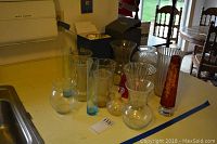 Ten glass vases arranged on a yellow surface, showing varying heights and designs including one red floral etching vase.