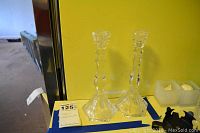 Pair of clear Tiffany candlesticks on a table against a yellow wall with visible faceted bases and sculpted stems.
