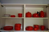 Red Gerz German stoneware pieces including plates, bowls, cups and pitchers arranged inside a cabinet.